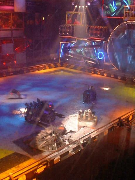 Several combat robots competing inside the brightly lit Robot Wars arena, viewed from above behind the safety barrier.