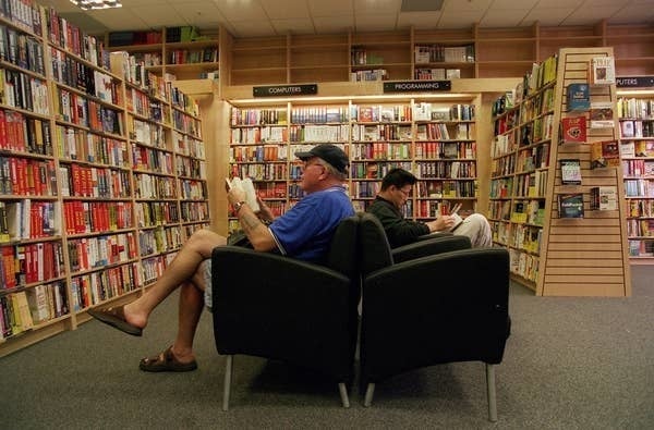 Two customers seated in black armchairs reading books between tall, densely stocked shelves inside a Borders bookshop.