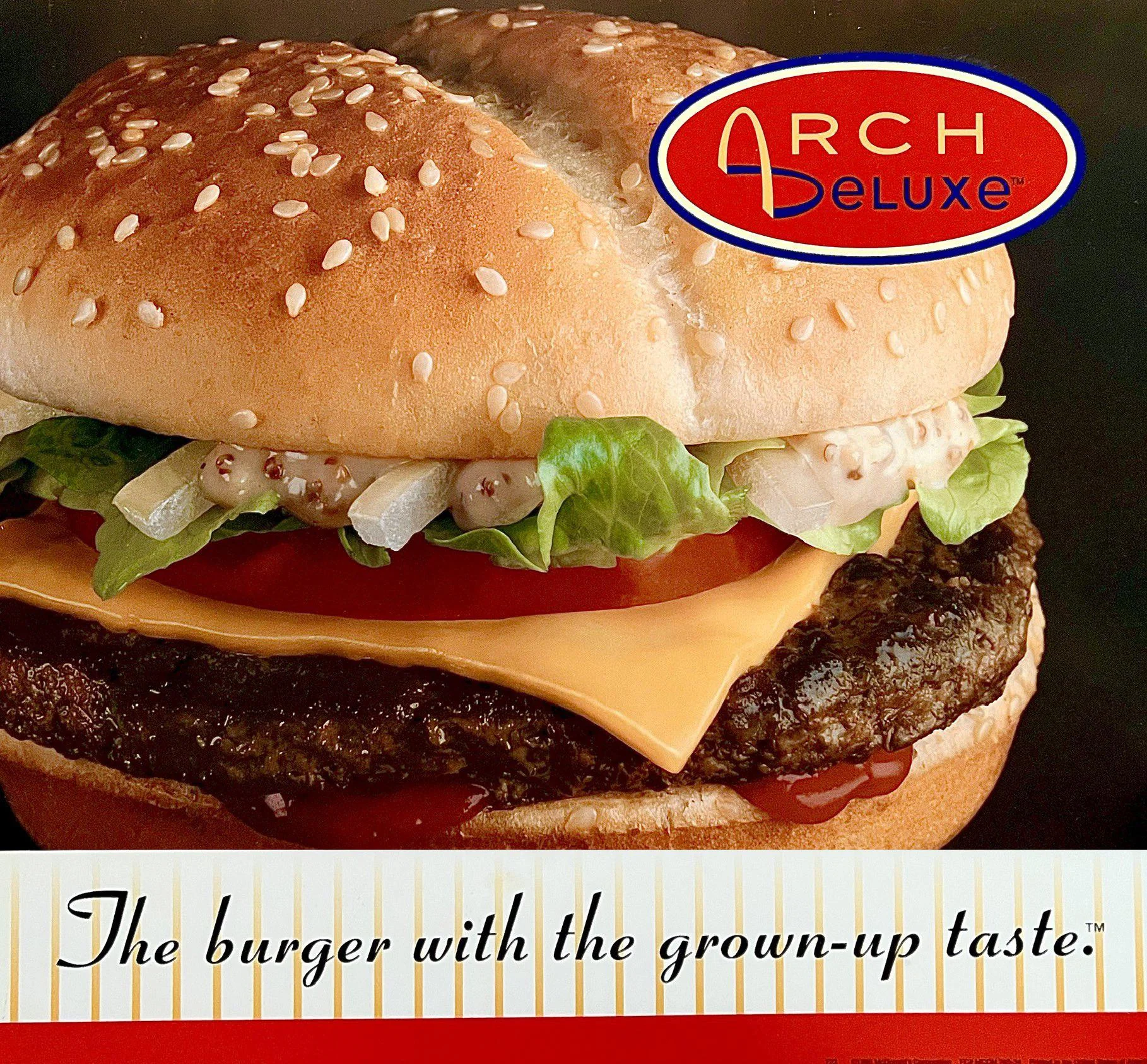 McDonald's Arch Deluxe advertisement showing a close-up burger beneath its red logo and the slogan 'The burger with the grown-up taste.'