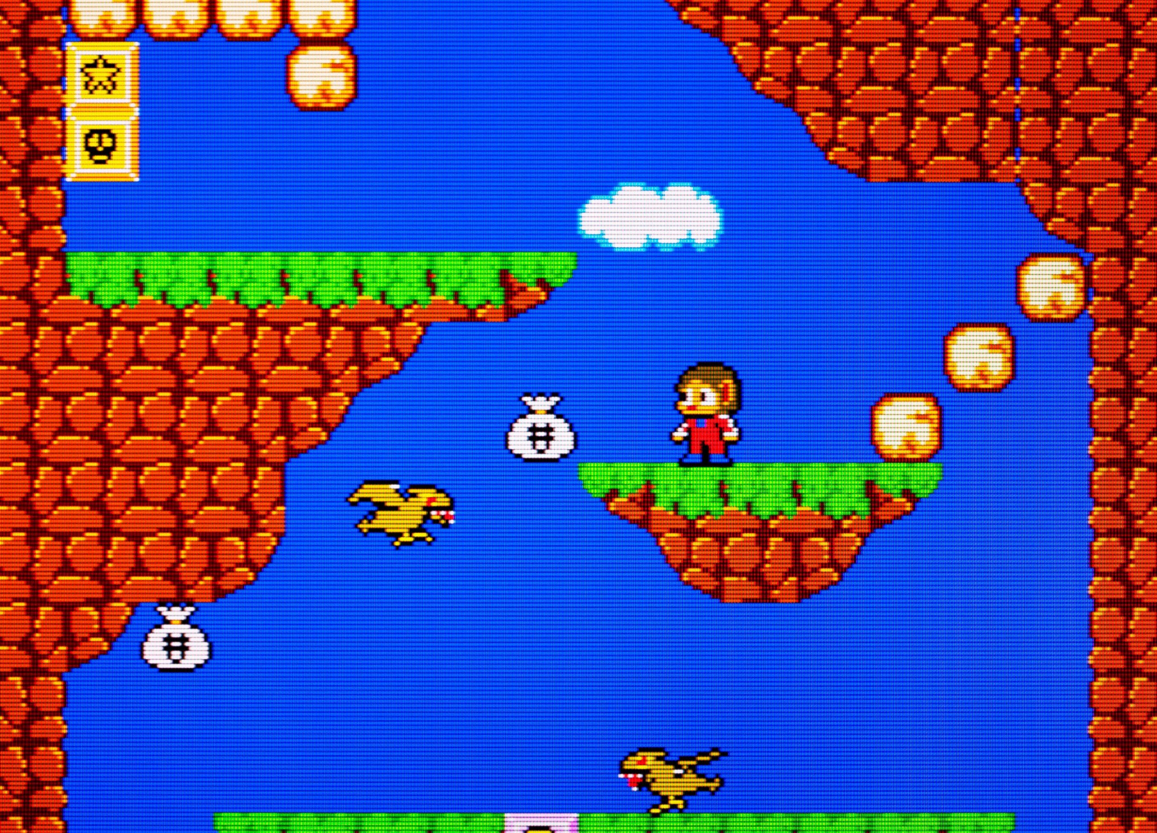 Pixel-art gameplay from Alex Kidd in Miracle World, showing Alex on a grassy rock platform surrounded by coins, flying creatures and money bags.