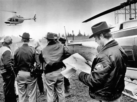 Black-and-white photograph of investigators examining a map beside helicopters during a search operation.