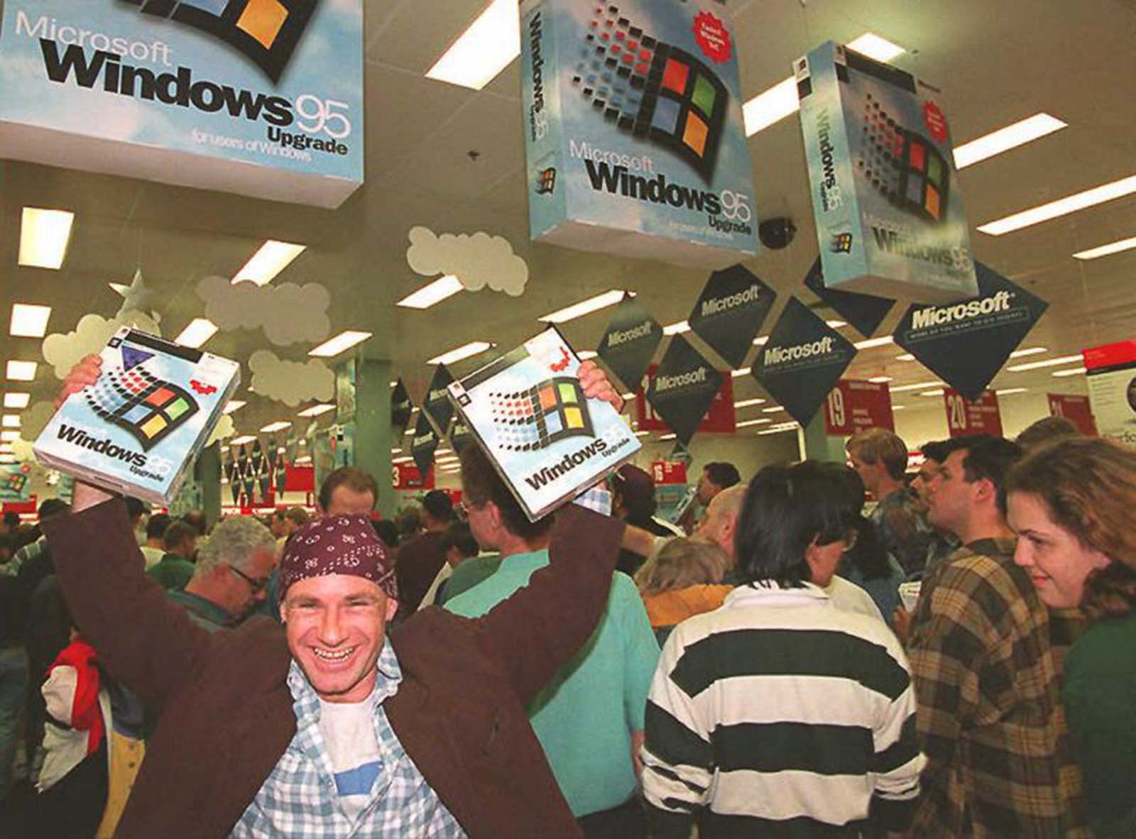 Crowded shop at the Windows 95 launch, with customers holding large software boxes beneath hanging Windows 95 displays.