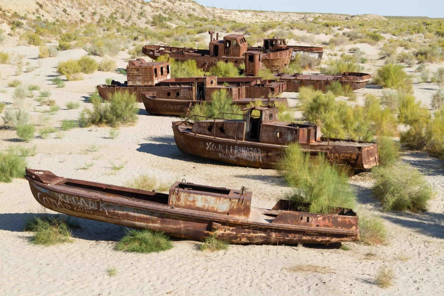 Several rusted abandoned boats scattered among sand dunes and scrub on the former Aral Sea bed.