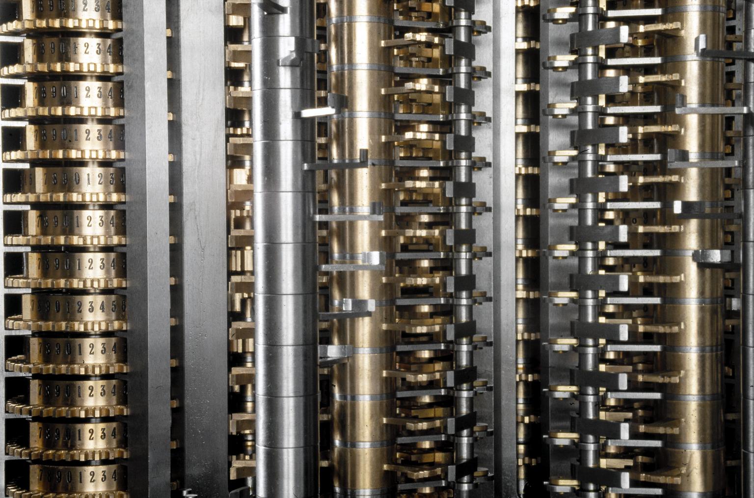Close-up of the Difference Engine's densely arranged brass numbered wheels, gears and steel shafts.