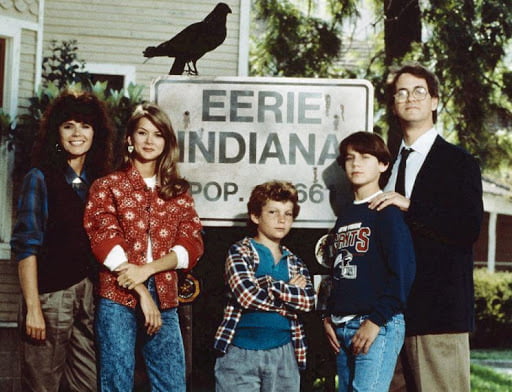 Five Eerie, Indiana cast members posed around the town sign with a black crow perched above them.