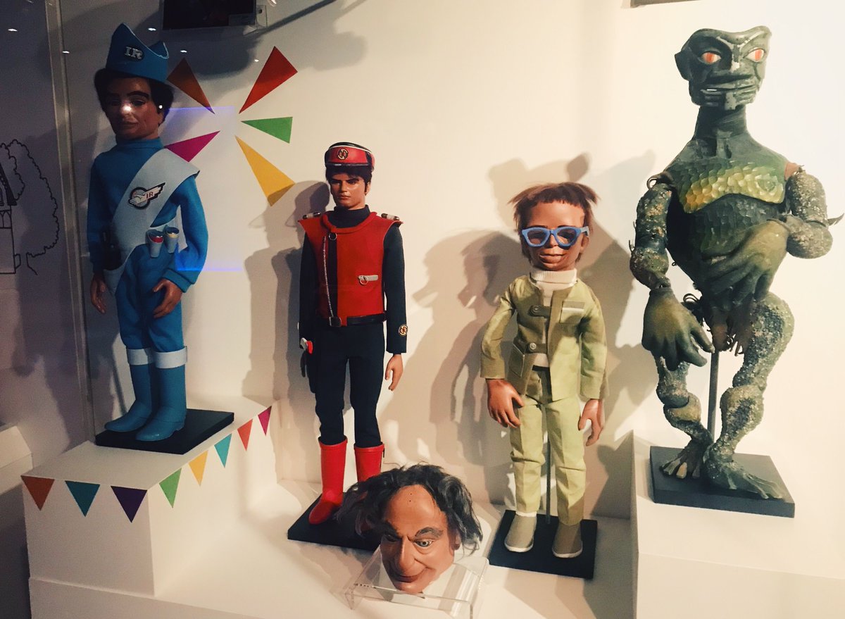 Museum display of Gerry Anderson puppets and a green creature, including a bespectacled Joe 90 figure.