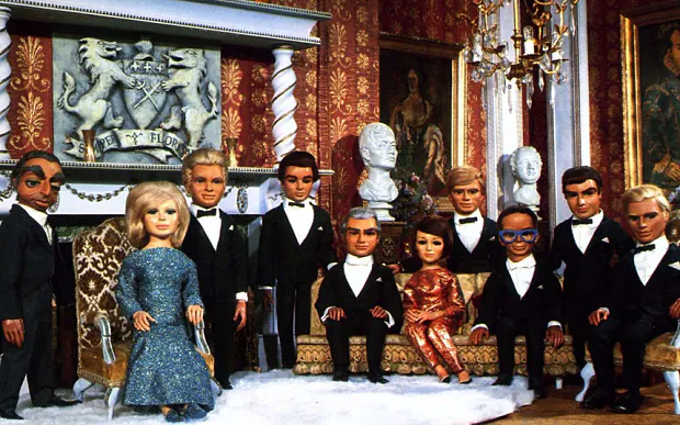 Formal group portrait of Gerry Anderson puppet characters dressed in evening wear inside an ornate room.