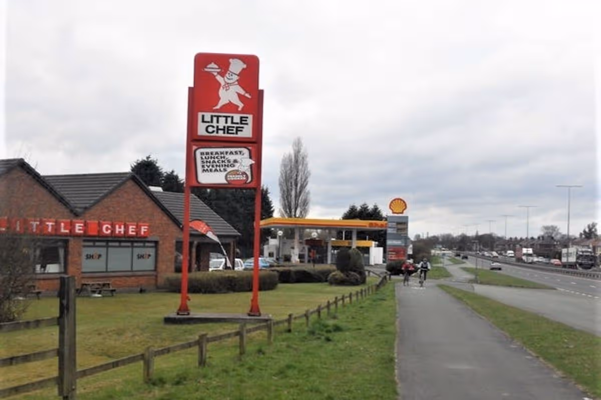 Little Chef restaurant and tall roadside sign beside a Shell petrol station and dual carriageway.