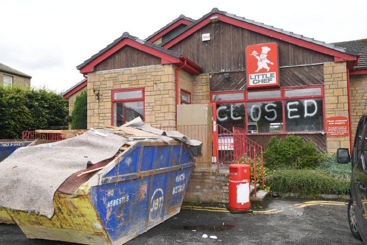 Abandoned Little Chef building with 'closed' painted across its windows and a skip outside.