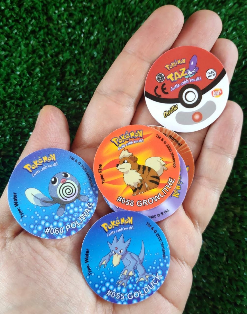 Hand holding several Pokémon Tazos featuring Poliwag, Growlithe and Golduck.