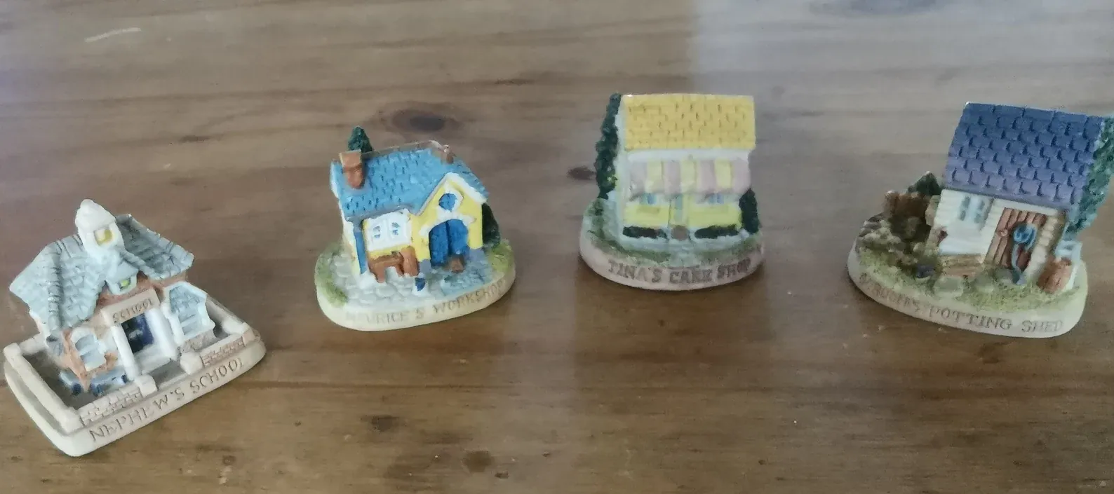 Four miniature Tetley Tea Folk village buildings labelled Nephew's School, Maurice's Workshop, Tina's Cake Shop and Gordon's Potting Shed.