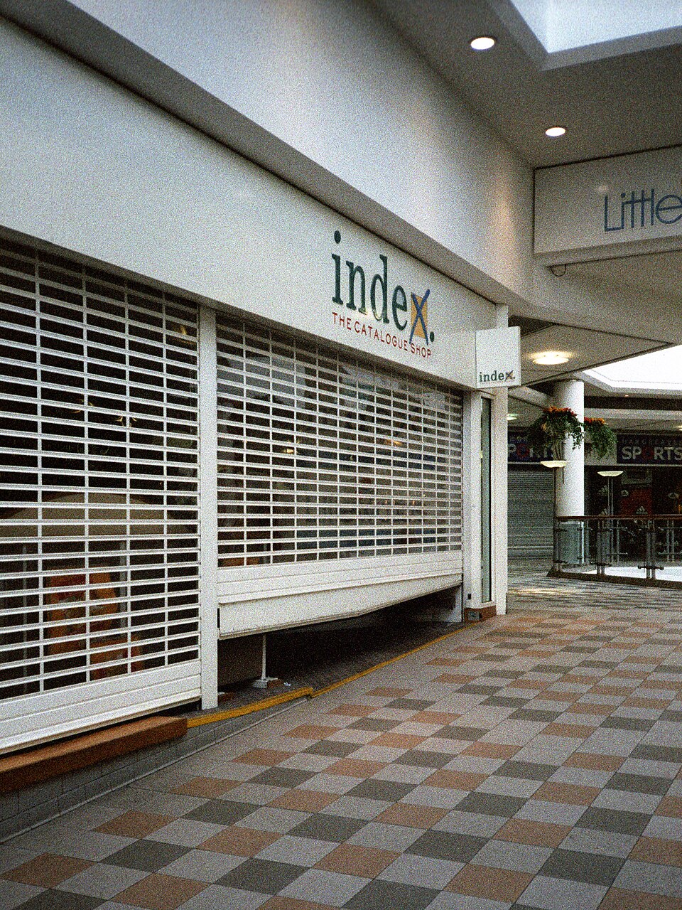 Closed Index catalogue shop with metal security grilles pulled across its frontage in a shopping-centre corridor.