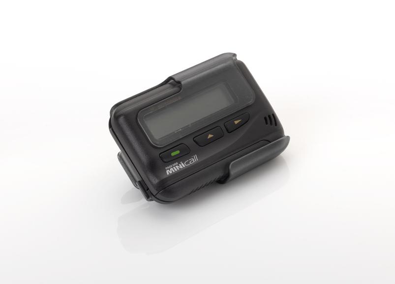 Black Motorola Pager One Minicall pager on a white background, shown at an angle with a blank screen, three front buttons and a curved lower clip or cradle-like attachment.