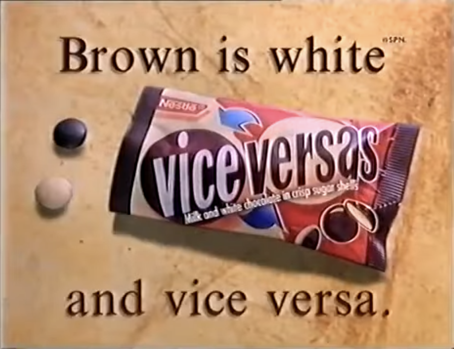 Advertisement-style image showing a Vice Versas candy packet on a beige background, with one dark and one white round candy beside it and the text “Brown is white” above and “and vice versa.” below.