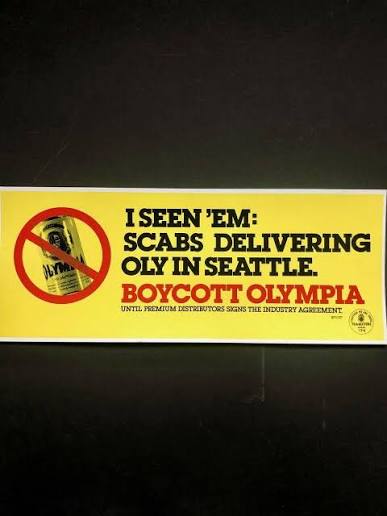 Yellow rectangular sign with a crossed-out Olympia beer can and the text “I SEEN ’EM: SCABS DELIVERING OLY IN SEATTLE. BOYCOTT OLYMPIA.”