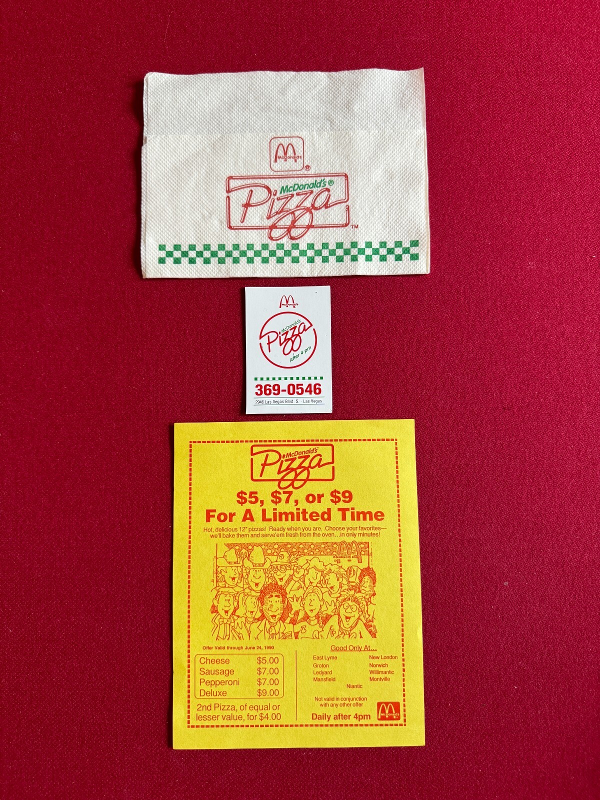 Three McDonald's Pizza paper items arranged on red fabric: a white napkin with a Pizza logo and green checker stripe, a small ticket marked “After 4 pm” and “369-0546,” and a yellow limited-time pizza coupon listing prices and locations.