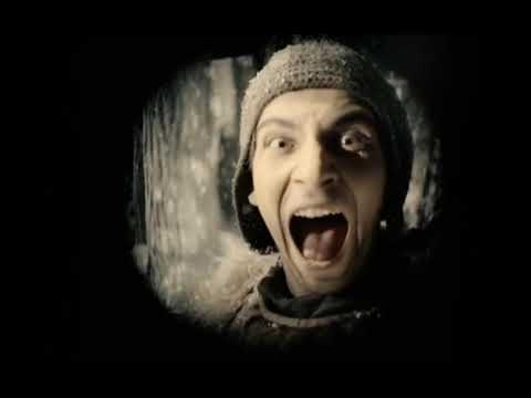 A man in a knitted cap and scarf faces the camera with his mouth open, shown inside a small circular vignette against a black background; blurred trees are behind him.