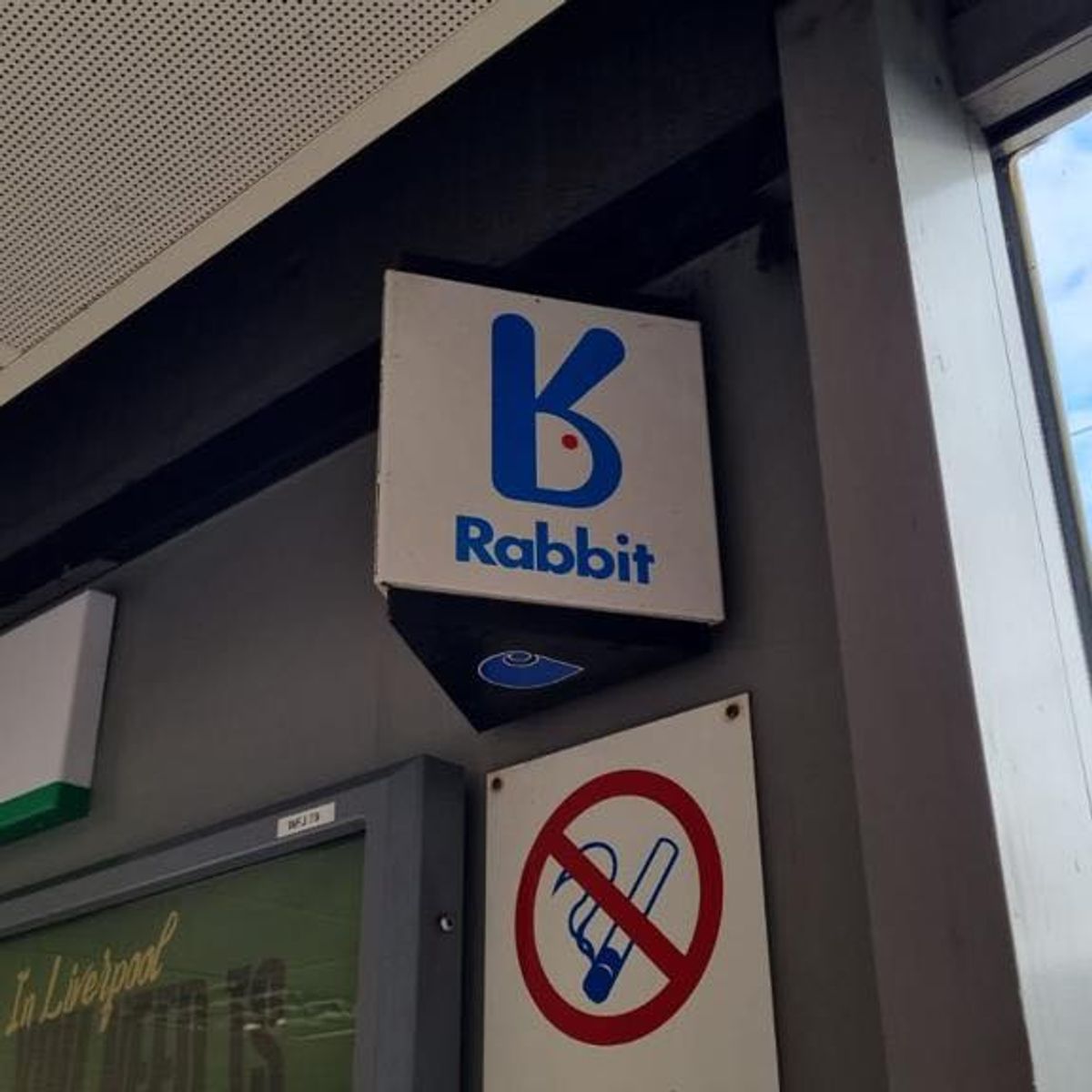 Photograph of a square Rabbit sign with a blue stylized rabbit logo and the word “Rabbit,” mounted indoors above a sign showing a crossed-out telephone handset symbol.