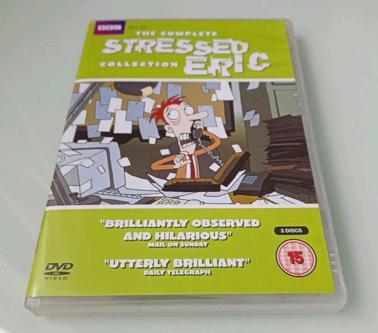 Photograph of a DVD case titled “The Complete Stressed Eric Collection,” showing an animated red-haired man at a desk covered in papers while holding a telephone.