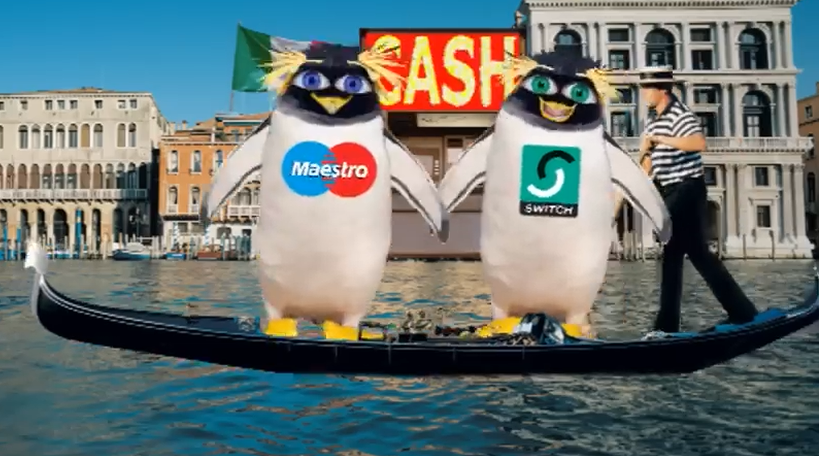 Two large penguin mascots stand in a gondola on a canal, one wearing a Maestro logo and the other a Switch logo, with a gondolier behind them and a large red “CASH” sign between buildings in the background.
