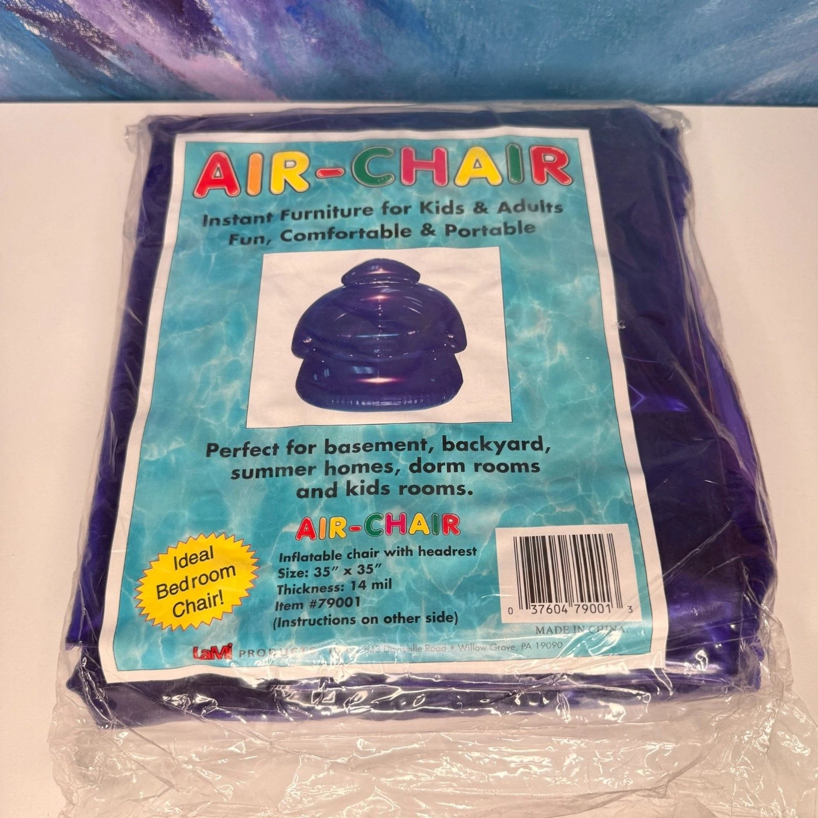 A folded dark purple inflatable chair in clear plastic packaging, with a printed Air-Chair label showing a purple chair and product text.
