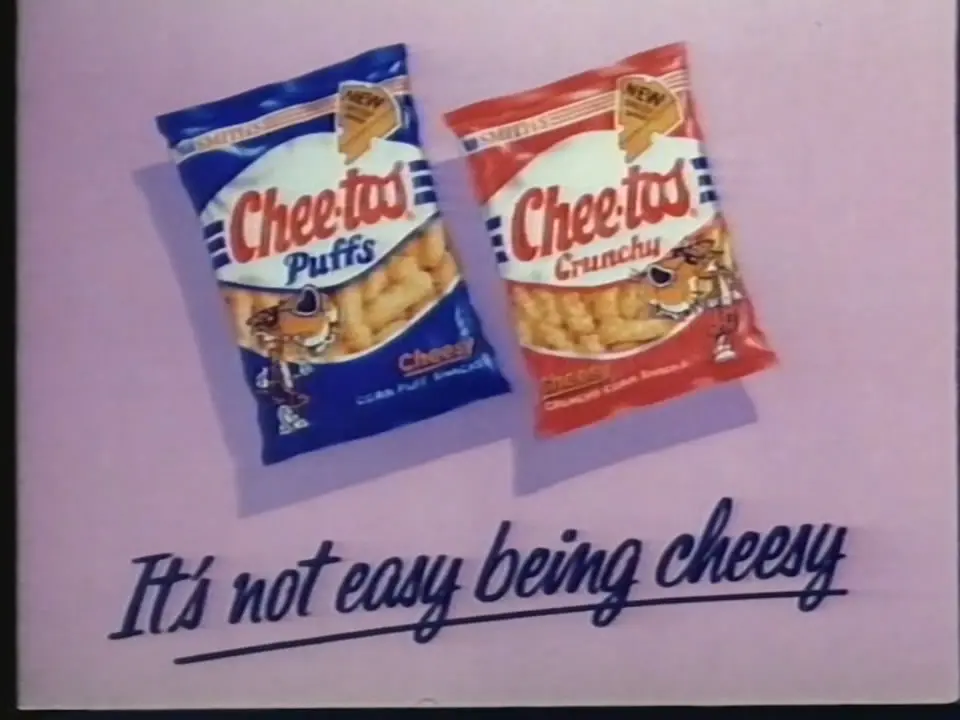 Pink advertising panel showing blue Cheetos Puffs and red Cheetos Crunchy packets, each featuring Chester Cheetah, above the slogan “It’s not easy being cheesy.”