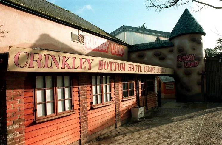 Exterior of a themed attraction building with a large sign reading “CRINKLEY BOTTOM HAUTE CUISINE” above red wooden cladding and windows; a round turret at right is marked “BLOBBY LAND.”