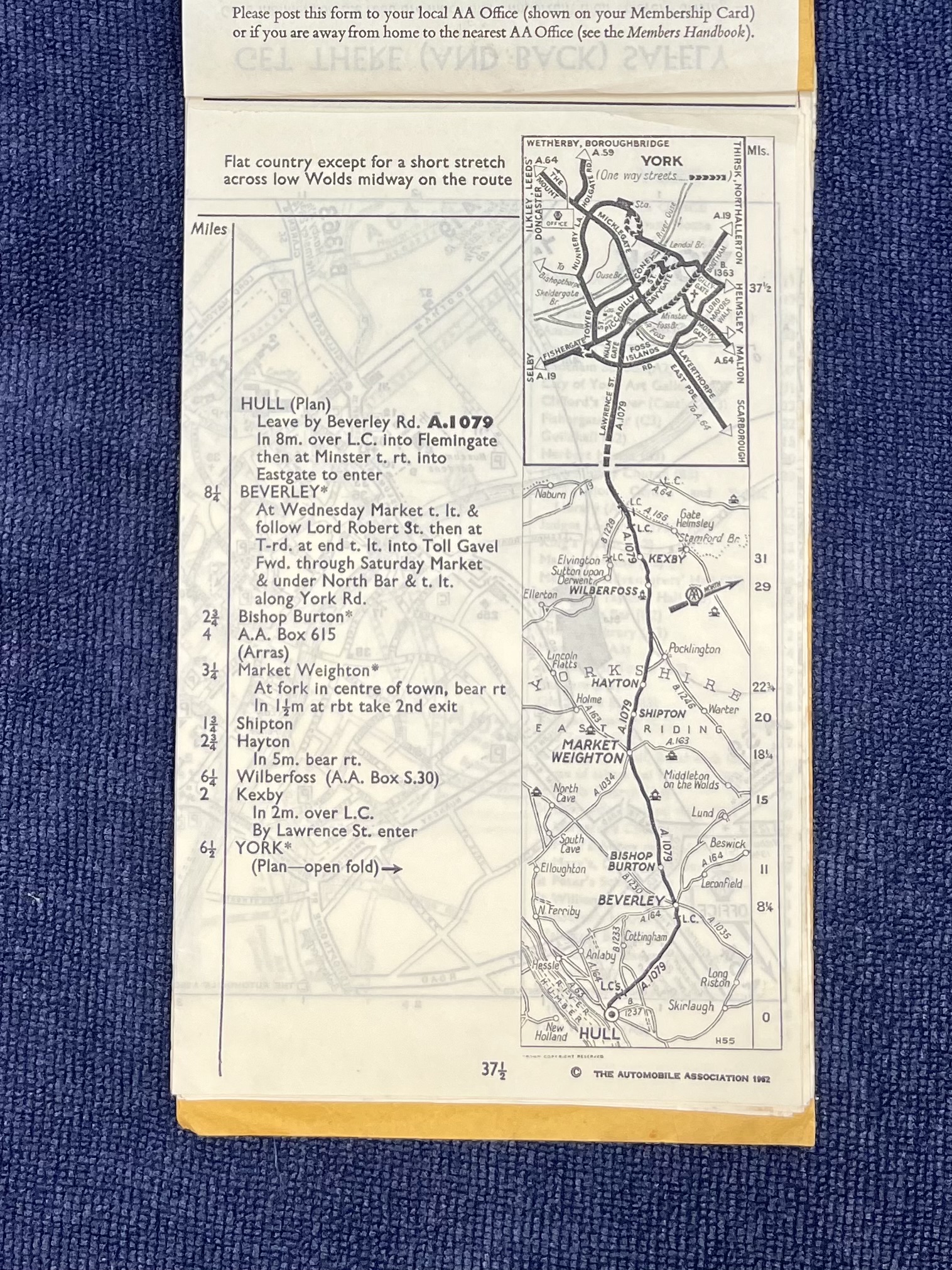 Open cream paper route sheet on dark blue textured fabric, with turn-by-turn directions and a vertical road map for the 37½-mile route from Hull through Beverley and Market Weighton to York; “The Automobile Association 1962” is printed along the bottom.