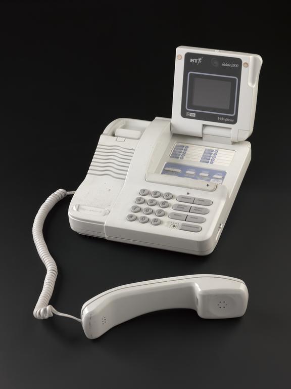 White BT Relate 2000 videophone photographed against a black background, with its small screen raised, keypad and controls visible, and the corded handset placed in front of the base.