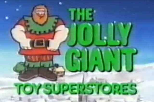Low-resolution television frame showing a cartoon giant in red and green winter clothing beside large green words reading “The Jolly Giant Toy Superstores,” against a snowy blue landscape.
