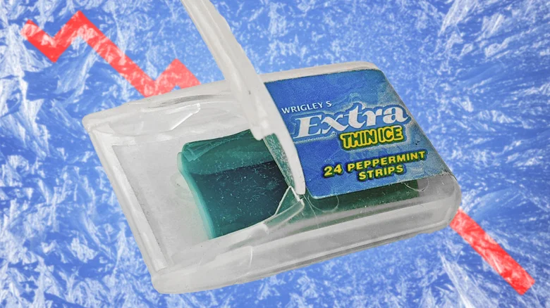 An open translucent plastic dispenser on a blue ice-textured background, containing a stack of turquoise rectangular strips. Its blue label reads “Wrigley’s Extra Thin Ice” and “24 Peppermint Strips.”