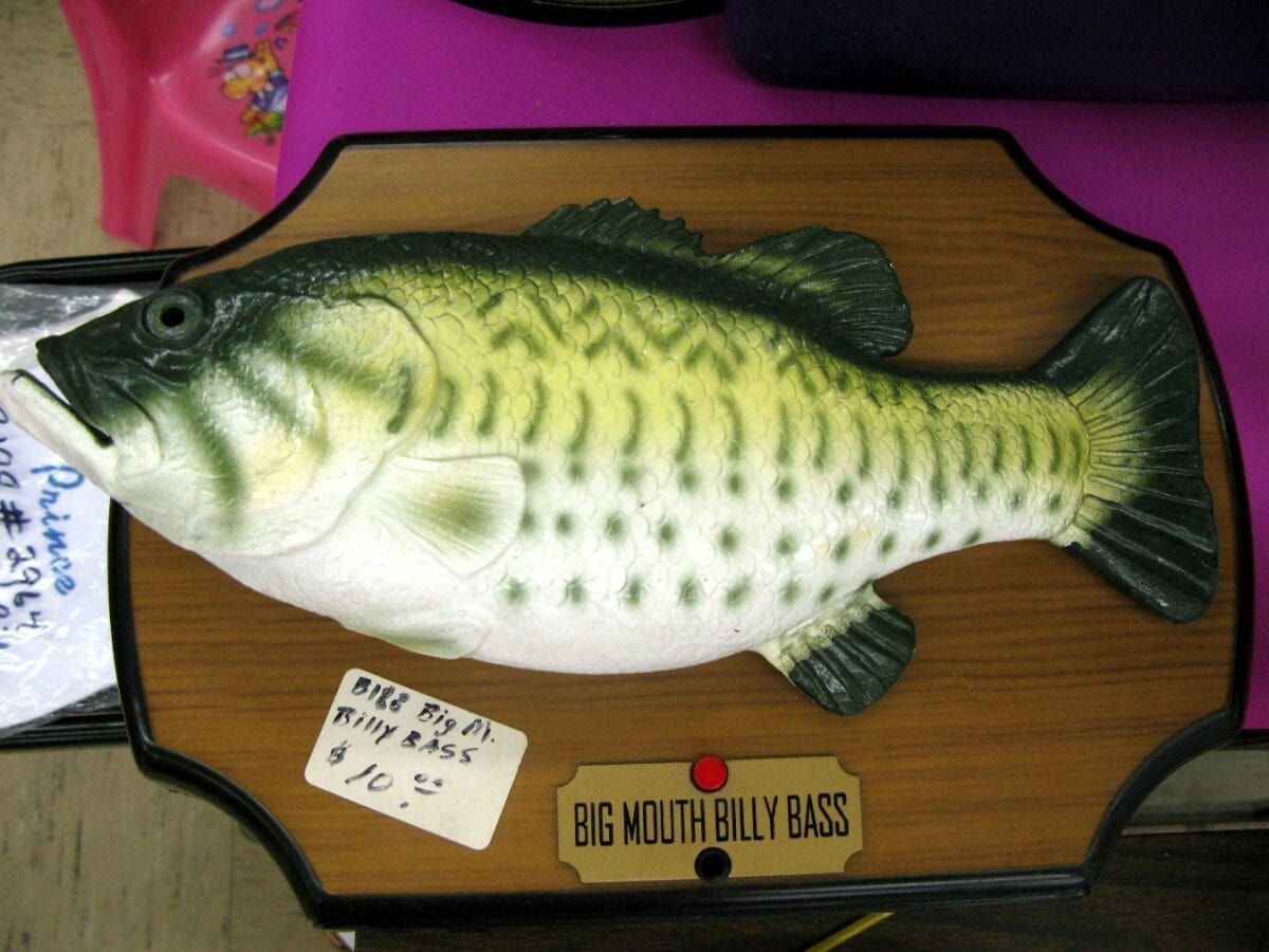 Green-and-yellow Billy Bass on a wood-effect plaque with a red button, nameplate and handwritten ten-dollar price sticker.