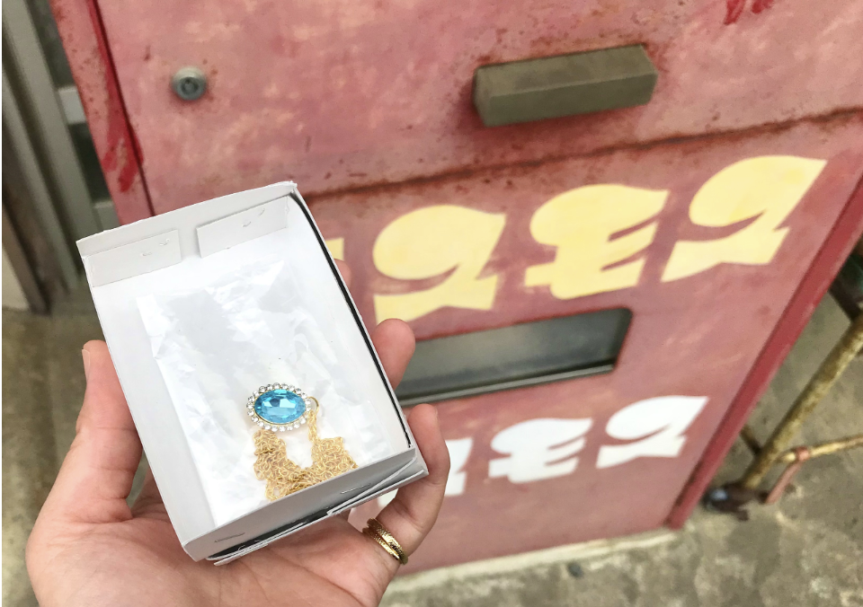A boxed toy necklace dispensed from a surviving Cosmos machine in Miyagi Prefecture, photographed in 2026. The purchase cost ¥100.