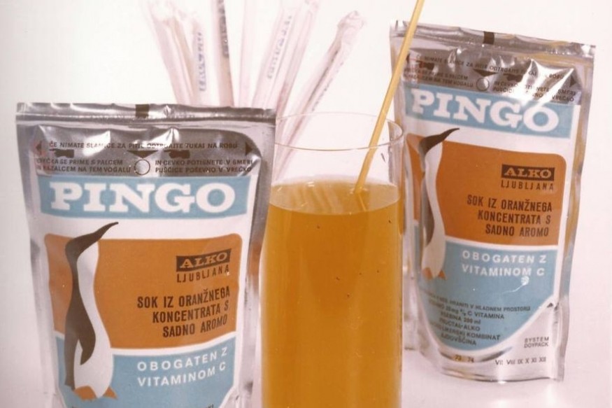 Original-style Pingo fruit drink pouches displayed alongside a glass of juice and drinking straws, recalling the familiar childhood ritual of piercing the foil packaging.