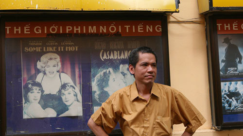 Nguyễn Quang Dũng standing outside Fansland Cinema beside framed film posters, including Some Like It Hot and Casablanca.