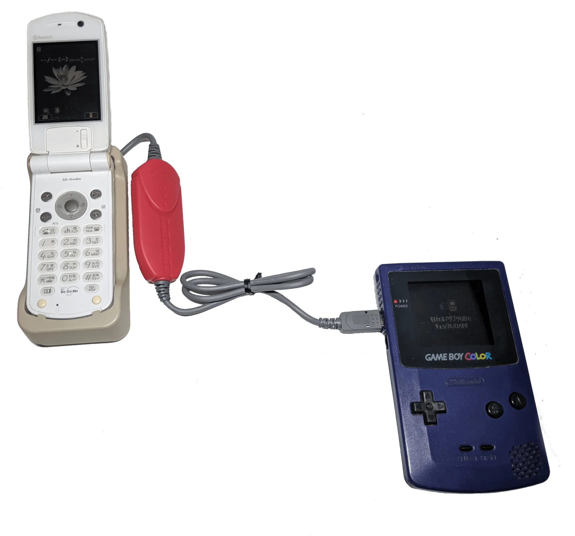 A blue Mobile Adapter GB linking a translucent Game Boy Color to a Japanese mobile phone beside a Pokémon Crystal cartridge.