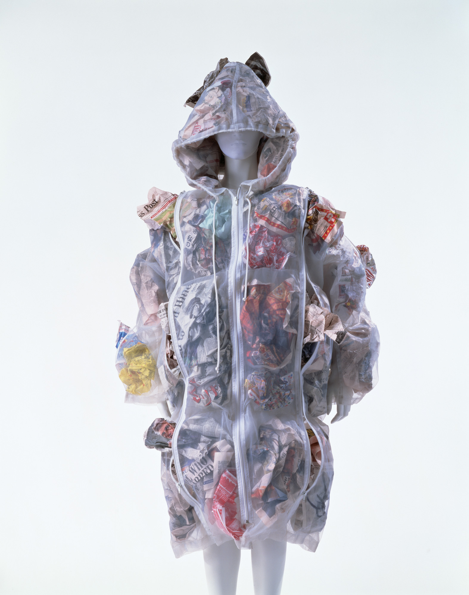Translucent hooded FINAL HOME coat on a mannequin, with its many zipped compartments filled with crumpled paper.