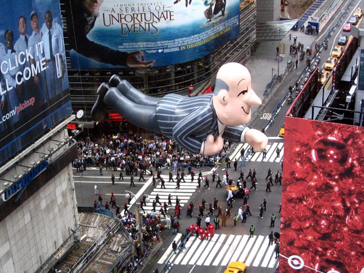 Large pinstriped butler balloon floats horizontally over handlers and crowds at a Times Square intersection, beneath billboards and beside a red Target display.