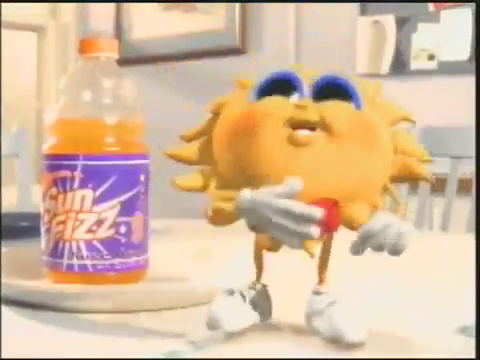 Yellow sun character with blue eyelids, red bowtie, gloves and white trainers stands on a kitchen table beside an orange drink bottle labelled Sun Fizz.