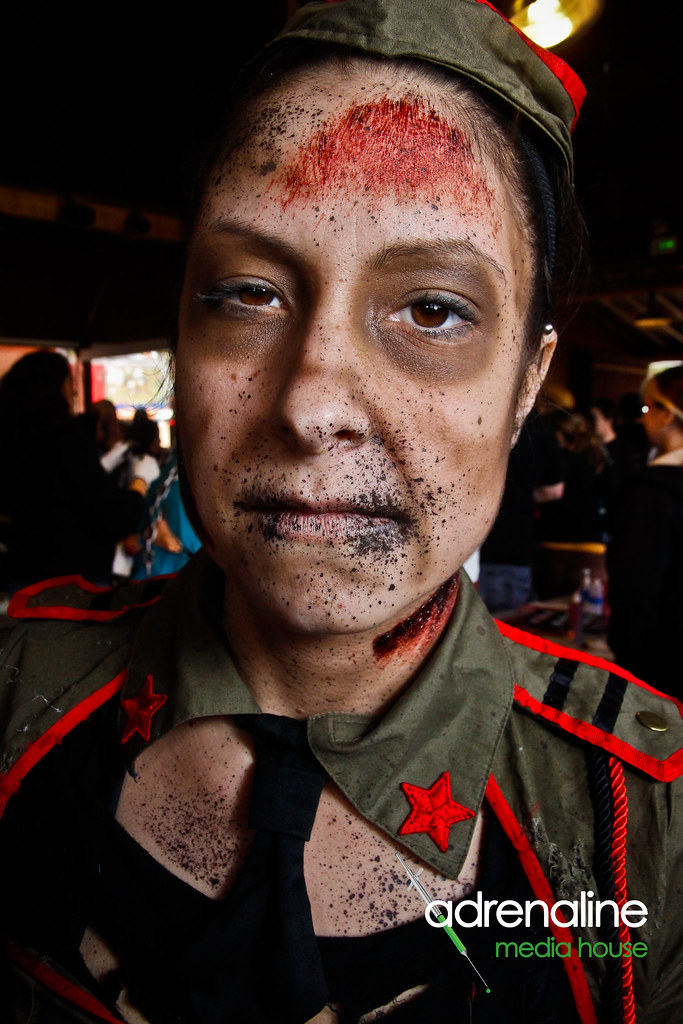 A participant wears theatrical zombie makeup, a green military-style costume and red star patches; an Adrenaline Media House watermark appears at the lower right.