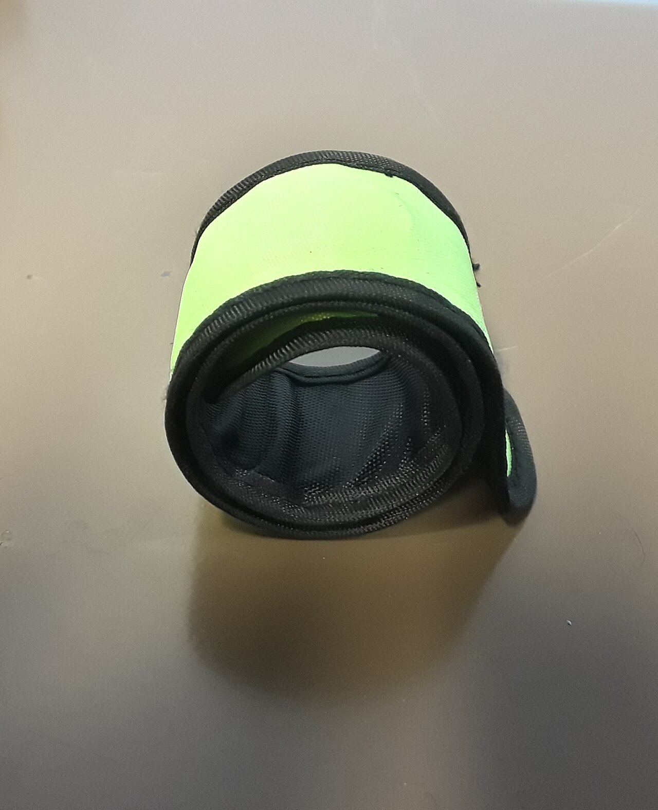 A neon-green and black fabric-covered slap bracelet rests coiled into overlapping loops on a plain surface.