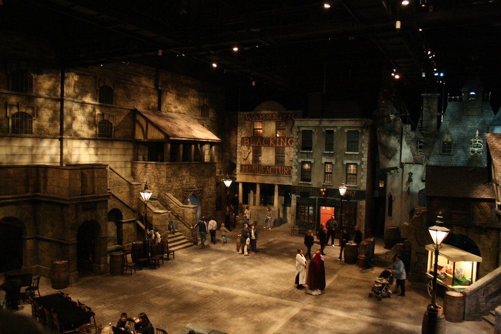Visitors stand among lamplit mock Victorian shopfronts beneath an exposed indoor roof at Dickens World.