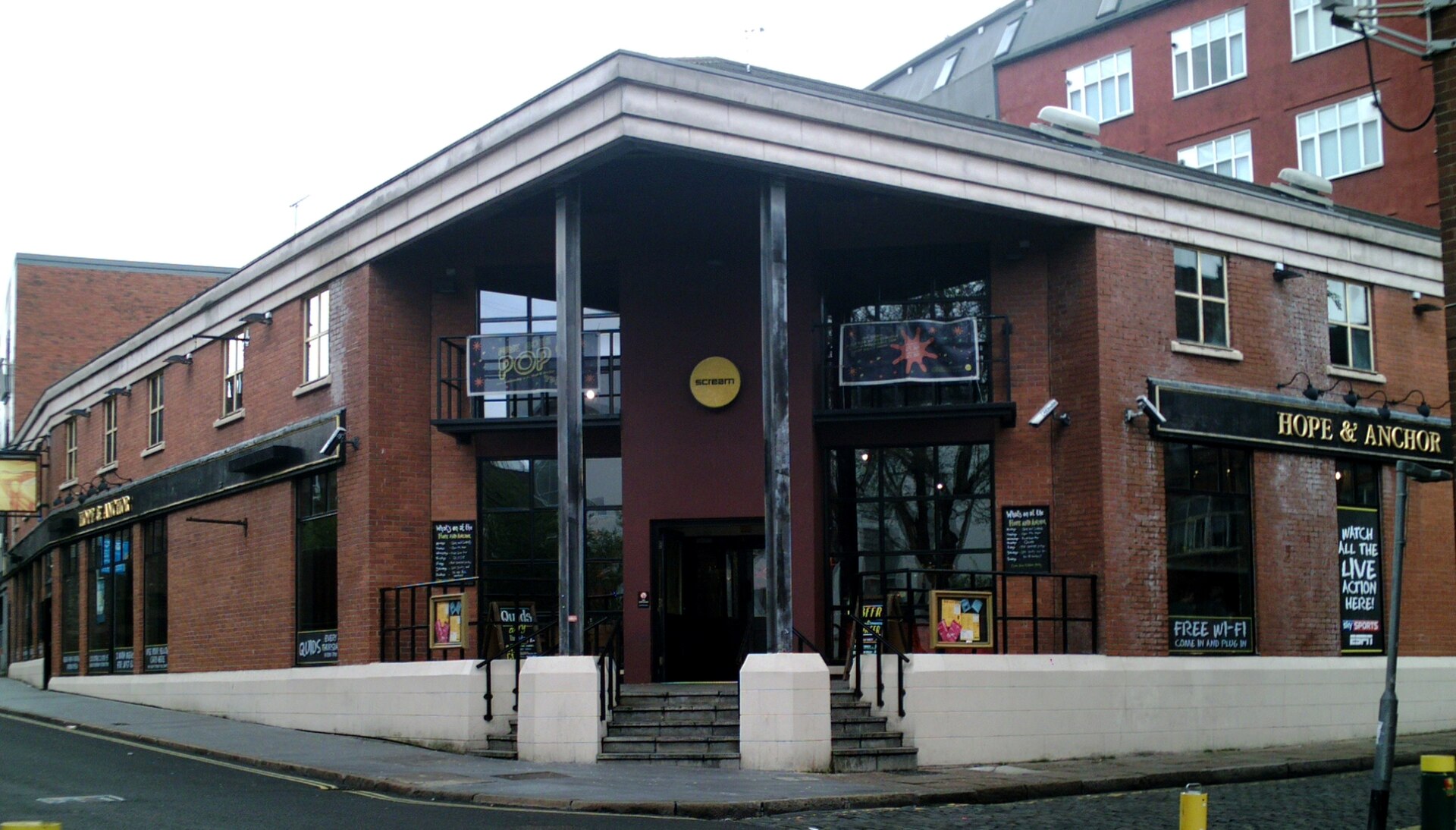 Red-brick Hope & Anchor pub with steps to a recessed entrance, gold name lettering and a small round yellow Scream sign.