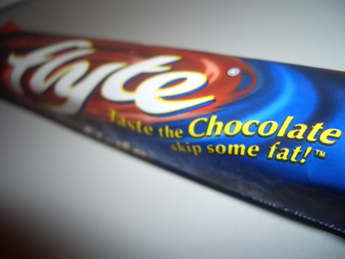 A blue-and-red Flyte wrapper lies diagonally on a pale surface, showing the yellow slogan “Taste the Chocolate… skip some fat!”
