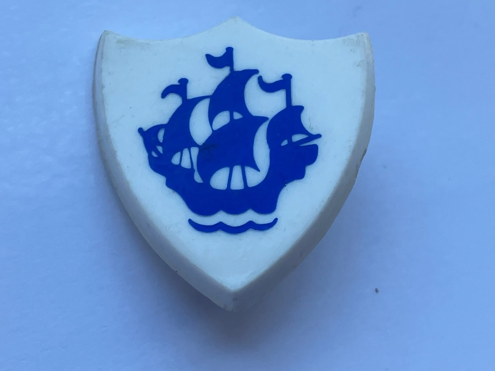 Blue-and-white shield graphic containing a large blue sailing ship with four sails, three small flags and stylised waves.