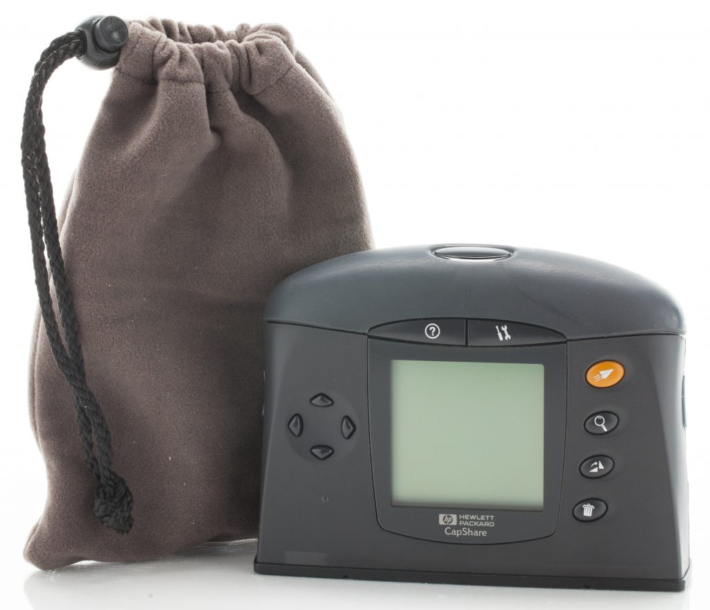 A dark grey HP CapShare scanner with a blank display and orange button stands beside its drawstring carrying pouch.