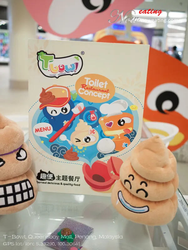 Upright T-Bowl menu printed with the words “Toilet Restaurant Concept,” Chinese text and cartoon bathroom-themed characters. Three brown plush toys shaped like coiled feces sit around it, with large colorful character figures blurred behind.