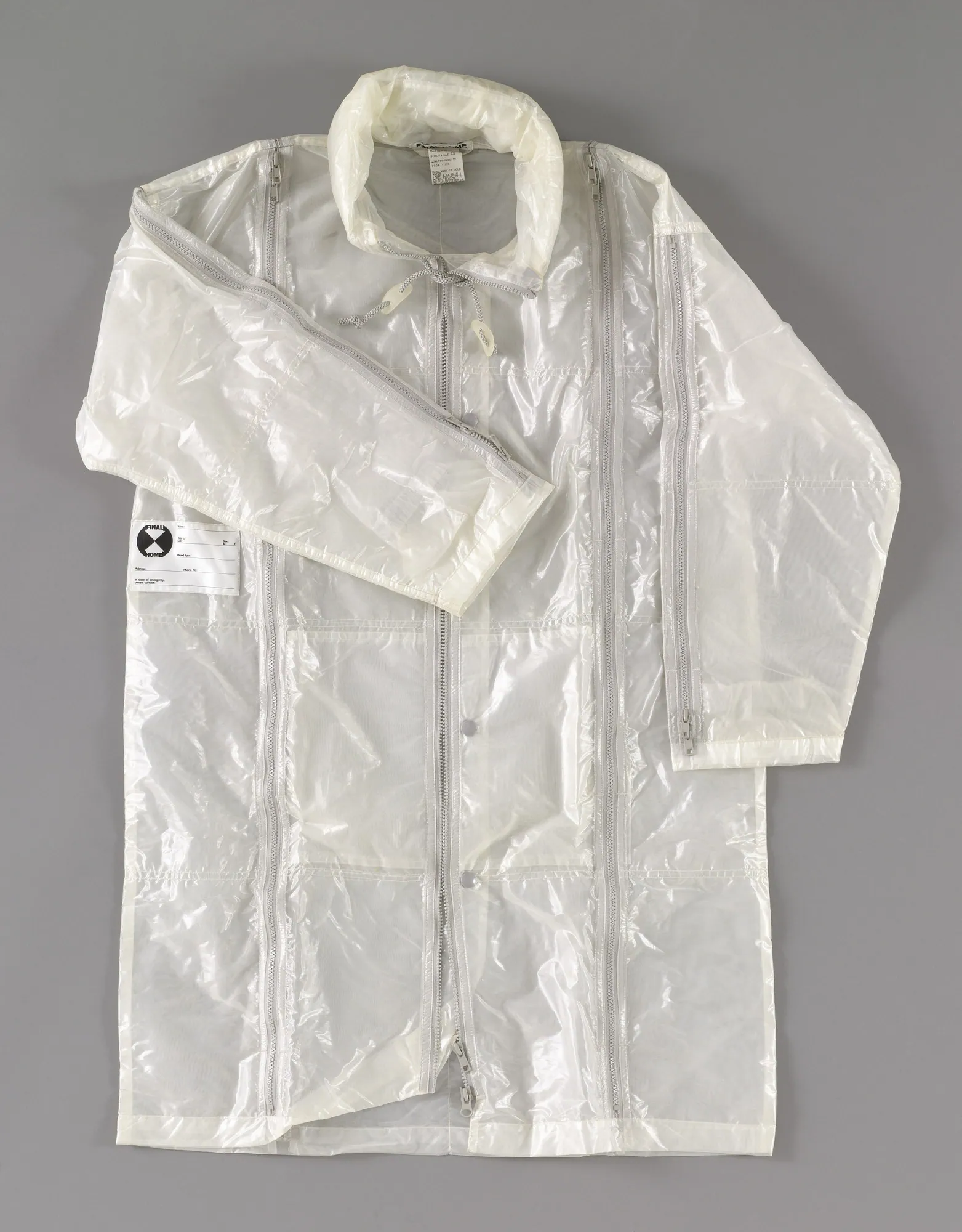 White translucent nylon parka laid flat on grey, with a hood, long front zips and one sleeve folded across the chest.
