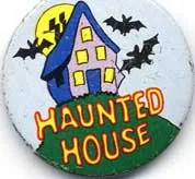 Round pale-blue badge showing a crooked blue and purple house with yellow windows, a yellow moon, three black bats and a black flying figure above the orange words “Haunted House.”