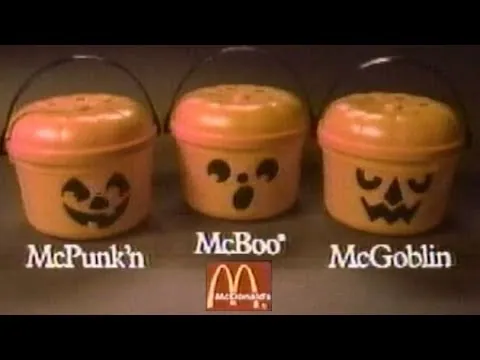 Low-resolution television frame with black borders showing three orange handled pumpkin buckets against a dark background. White labels beneath them read “McPunk’n,” “McBoo” and “McGoblin,” with a red McDonald’s logo below the center bucket.